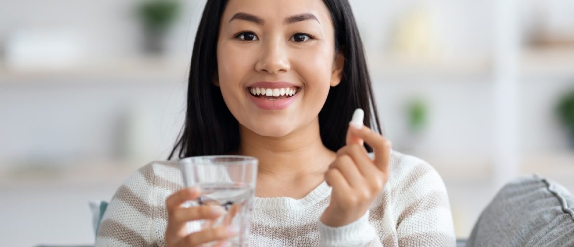 Beauty Supplements. Beautiful Young Asian Woman Holding Glass Of Water And Pill